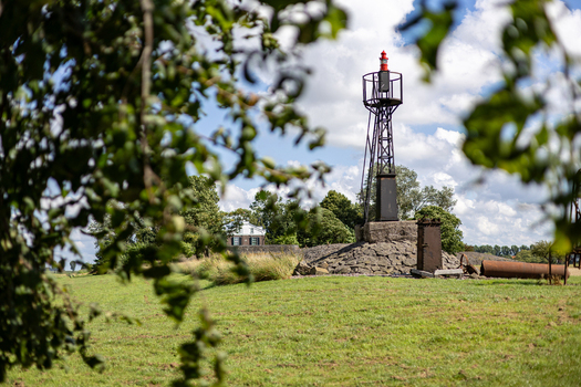 View of the historic beacon tower and Lichtwachterswoning Oud Kraggenburg surrounded by green fields and trees under a cloudy sky in Kraggenburg Flevoland Netherlands.