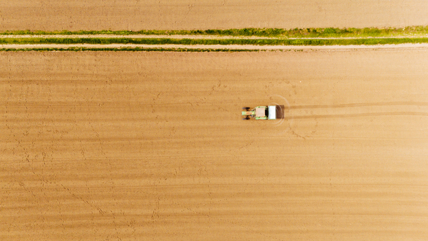 Aerial view of a lone tractor carving lines across a vast dry field bisected by a vibrant green strip of vegetation Sremska Mitrovica Vojvodina Serbia. Aerial view of a lone tractor carving lines across a vast dry field bisected by a vibrant green strip of vegetation Sremska Mitrovica Vojvodina Serbia.