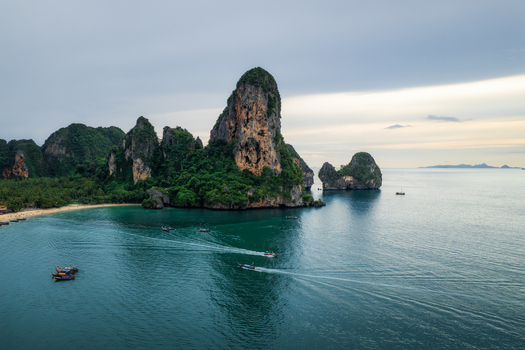 Aerial view of Railay Beach with limestone cliffs turquoise water and traditional long tail boats moving across the sea in Ao Nang Krabi Thailand.