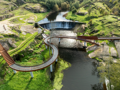 Aerial view of Acude da Ribeira featuring a winding pedestrian bridge and a small dam over the river surrounded by rocky green hills in Ervedal Coimbra Portugal. Aerial view of Acude da Ribeira featuring a winding pedestrian bridge and a small dam over the river surrounded by rocky green hills in Ervedal Coimbra Portugal.
