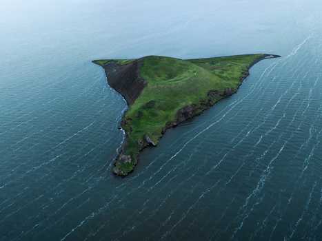 Aerial view of a verdant triangular island rising from the waters its slopes a stark contrast of dark volcanic rock and bright green grass Myvatn Þingeyjarsveit Iceland. Aerial view of a verdant triangular island rising from the waters its slopes a stark contrast of dark volcanic rock and bright green grass Myvatn Þingeyjarsveit Iceland.