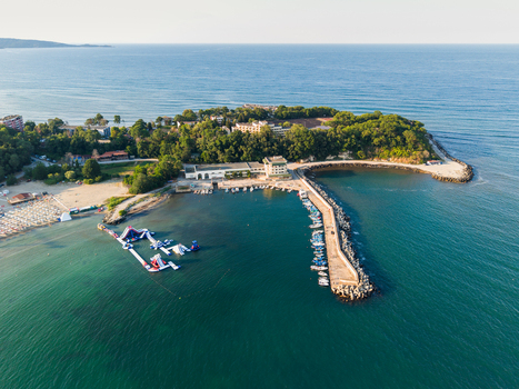 Aerial view of the coastline at Kiten featuring a breakwater small boats a sandy beach with an inflatable water park and lush green trees in Kiten Burgas Bulgaria. Aerial view of the coastline at Kiten featuring a breakwater small boats a sandy beach with an inflatable water park and lush green trees in Kiten Burgas Bulgaria.