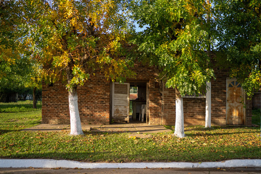 View of a rustic brick house with white painted tree trunks in the foreground and autumn foliage in Guaviravi Corrientes Province Argentina.