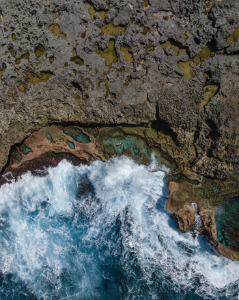 Aerial view of the rugged coastline where the churning turquoise sea clashes with the jagged sun baked rocks Lifou New Caledonia.