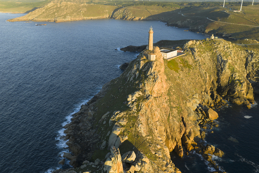 Aerial view of the historic Cabo Vilan lighthouse perched on rugged rocky cliffs overlooking the Atlantic Ocean in Galicia Spain.