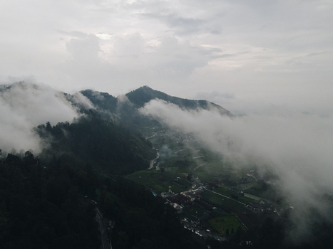 Aerial view of misty mountains and a valley village partially covered by thick white clouds under an overcast sky in Tawangmangu Central Java Indonesia.