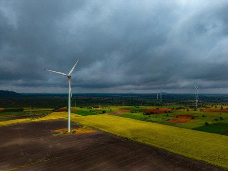 Aerial view of wind turbines standing in vast agricultural fields under a dramatic cloudy sky in the rural landscape of Hampi Karnataka India.