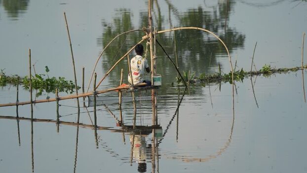 View of a fisherman using a traditional lift net in Bogura Bangladesh.