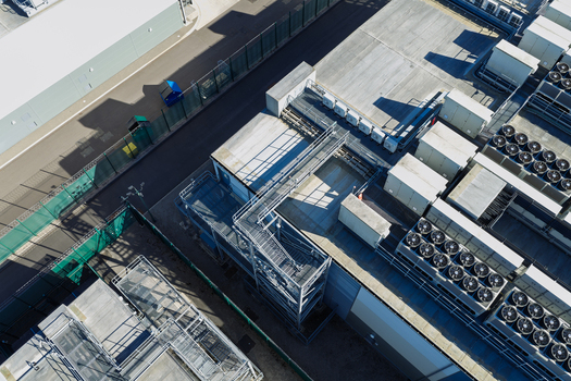 Aerial view of a data center roof featuring rows of industrial HVAC cooling units metal staircases and security fencing in the United Kingdom.