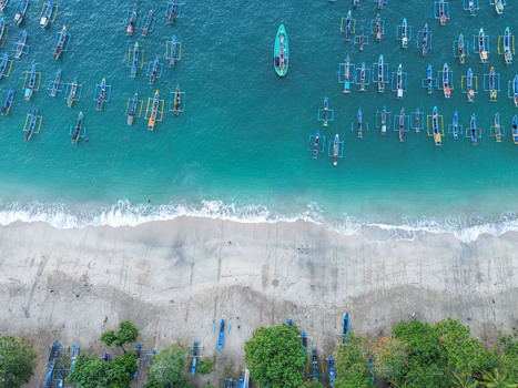 Aerial view of Papuma Beach with numerous traditional fishing boats in turquoise waters and on the sandy shore surrounded by lush green vegetation in Jember East Java Indonesia. Aerial view of Papuma Beach with numerous traditional fishing boats in turquoise waters and on the sandy shore surrounded by lush green vegetation in Jember East Java Indonesia.
