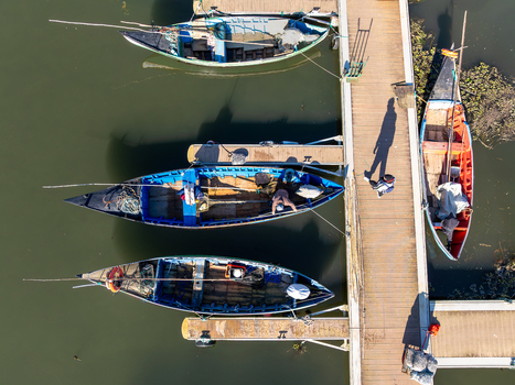 Aerial view of fishing boats in the harbor their vibrant colors contrasting against the dark water as a lone figure strolls along the wooden pier Porta de Abrigo da Torreira Aveiro Portugal. Aerial view of fishing boats in the harbor their vibrant colors contrasting against the dark water as a lone figure strolls along the wooden pier Porta de Abrigo da Torreira Aveiro Portugal.