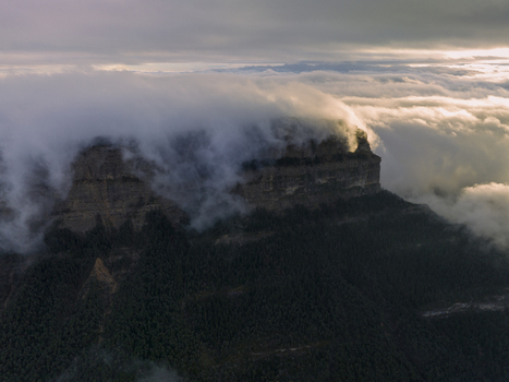 Aerial view of Pyrenees mountains shrouded in thick clouds above dense pine forests during golden hour in Spain. Aerial view of Pyrenees mountains shrouded in thick clouds above dense pine forests during golden hour in Spain.