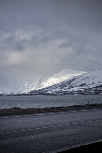 View of snow covered mountains and a calm fjord under a dramatic overcast sky from a roadside Kvaloya Troms Norway. View of snow covered mountains and a calm fjord under a dramatic overcast sky from a roadside Kvaloya Troms Norway.