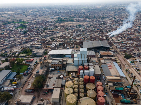 Aerial view of an industrial facility featuring large storage tanks and factory buildings with smoke rising from chimneys situated within the urban landscape of Multan Punjab Pakistan.