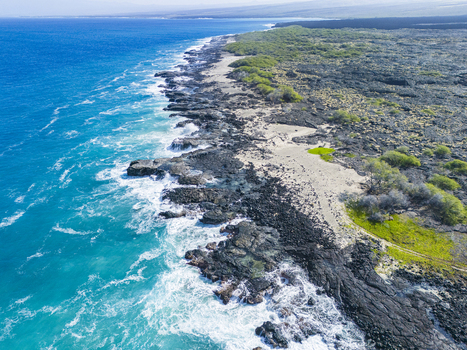 Aerial view of Kalaemamo coastline featuring black volcanic rock formations turquoise ocean waves and green coastal vegetation under a clear sky Hawaii County Hawaii United States. Aerial view of Kalaemamo coastline featuring black volcanic rock formations turquoise ocean waves and green coastal vegetation under a clear sky Hawaii County Hawaii United States.
