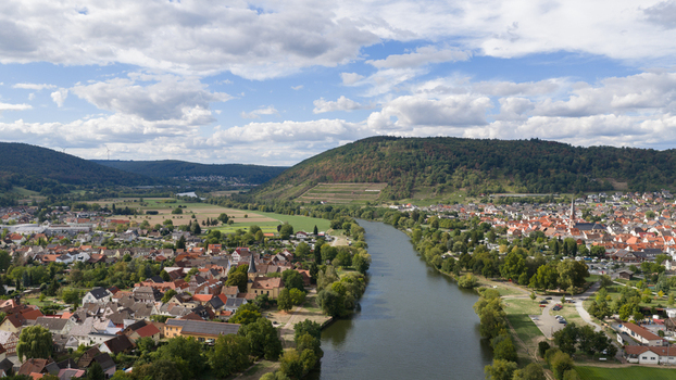 Aerial view of the town of Kleinheubach along the Main river surrounded by green hills and agricultural fields under a blue sky with clouds in Kleinheubach Bavaria Germany.
