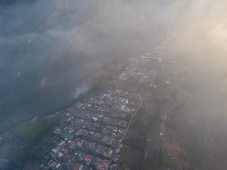Aerial view of Wonotoro village nestled in the mountains of East Java partially shrouded in mist during a golden sunset in Sukapura East Java Indonesia.