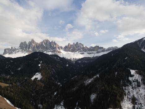 Aerial view of the snow capped Odle mountain peaks in Val di Funes with dense evergreen forests under a cloudy sky Funes Trentino Alto Adige Italy.
