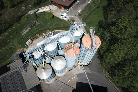 Aerial view of the Moulin de la Vaux industrial grain silos surrounded by lush green forest and a flowing river in Aubonne Vaud Switzerland. Aerial view of the Moulin de la Vaux industrial grain silos surrounded by lush green forest and a flowing river in Aubonne Vaud Switzerland.