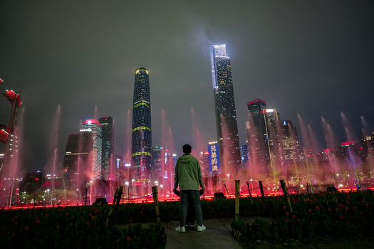 Guangzhou China 24 February 2024 View of a person standing before a vibrant fountain show with illuminated skyscrapers in the city skyline at night. Guangzhou China 24 February 2024 View of a person standing before a vibrant fountain show with illuminated skyscrapers in the city skyline at night.