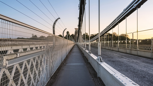 View of Clifton Suspension Bridge showing the pedestrian walkway with metal fencing and suspension cables under a clear sky at dusk in Bristol United Kingdom.