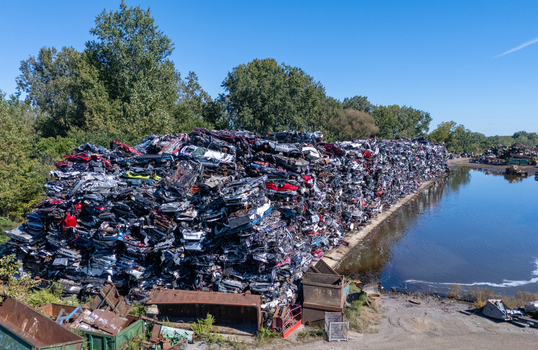 Aerial view of a scrap metal facility featuring massive stacks of crushed cars beside a body of water in Kalamazoo Michigan United States. Aerial view of a scrap metal facility featuring massive stacks of crushed cars beside a body of water in Kalamazoo Michigan United States.