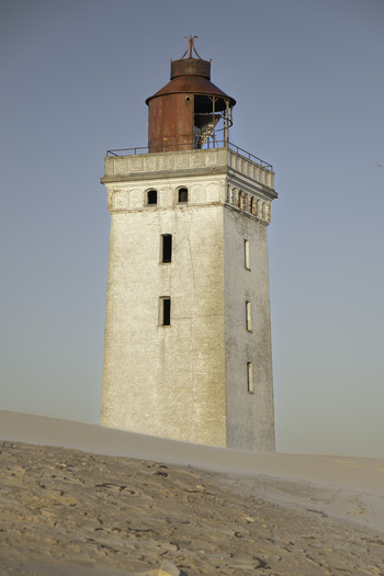 View of the historic Rubjerg Knude lighthouse with its white tower and red lantern room rising above the surrounding sand dunes Lokken Denmark. View of the historic Rubjerg Knude lighthouse with its white tower and red lantern room rising above the surrounding sand dunes Lokken Denmark.