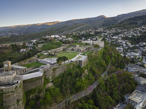 Aerial view of Gjirokaster Fortress with its historic stone walls clock tower and green courtyards overlooking the hillside city of Gjirokaster Gjirokaster County Albania. Aerial view of Gjirokaster Fortress with its historic stone walls clock tower and green courtyards overlooking the hillside city of Gjirokaster Gjirokaster County Albania.