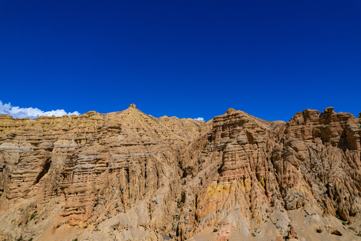 Aerial view of arid layered rock formations and steep mountain cliffs under a clear blue sky in Nepal.