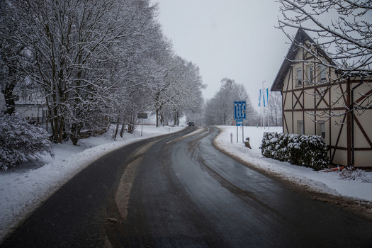 View of a snow covered road winding past a traditional half timbered house and trees under a winter sky in Austria. View of a snow covered road winding past a traditional half timbered house and trees under a winter sky in Austria.