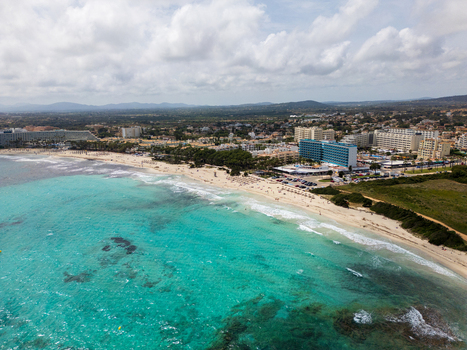 Aerial view of the turquoise waters and sandy beach with people relaxing near coastal hotels and resorts in Sa Coma Balearic Islands Spain. Aerial view of the turquoise waters and sandy beach with people relaxing near coastal hotels and resorts in Sa Coma Balearic Islands Spain.