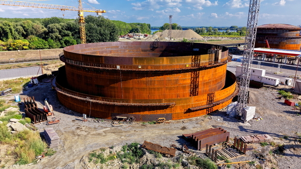 Aerial view of the assembly of a large industrial oil storage tank at a refinery construction site featuring rusted steel panels cranes and heavy machinery in Kovin Vojvodina Serbia. Aerial view of the assembly of a large industrial oil storage tank at a refinery construction site featuring rusted steel panels cranes and heavy machinery in Kovin Vojvodina Serbia.