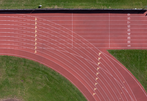 Aerial view of the red running track field with white lane markings and numbered lanes surrounded by green grass in Kalamazoo Michigan United States. Aerial view of the red running track field with white lane markings and numbered lanes surrounded by green grass in Kalamazoo Michigan United States.