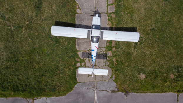 Serbia 11 April 2021 Aerial view of a small white propeller aircraft parked on a weathered concrete runway surrounded by green grass. Serbia 11 April 2021 Aerial view of a small white propeller aircraft parked on a weathered concrete runway surrounded by green grass.