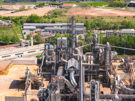 Aerial view of an industrial wood processing plant with complex piping tall chimneys and large piles of sawdust under bright sunlight in Jihlava Vysocina Region Czechia.