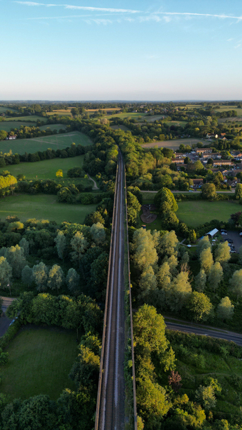 Aerial view of the historic Chappel Viaduct stretching through the lush green countryside of the Colne Valley surrounded by dense trees in Chappel England United Kingdom.