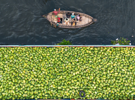 Dhaka Bangladesh 04 April 2026 Aerial view of a boat laden with vibrant green produce and a passenger boat cutting through the dark waters of a river. Dhaka Bangladesh 04 April 2026 Aerial view of a boat laden with vibrant green produce and a passenger boat cutting through the dark waters of a river.