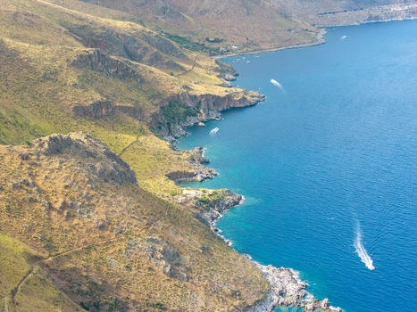 Aerial view of the rugged coastline of Riserva Naturale Orientata dello Zingaro with turquoise waters and small boats navigating the sea in San Vito Lo Capo Sicilia Italy. Aerial view of the rugged coastline of Riserva Naturale Orientata dello Zingaro with turquoise waters and small boats navigating the sea in San Vito Lo Capo Sicilia Italy.