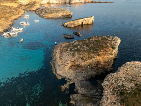 Aerial view of turquoise waters meet rugged cliffs and anchored boats in the Blue Lagoon Comino Malta. Aerial view of turquoise waters meet rugged cliffs and anchored boats in the Blue Lagoon Comino Malta.