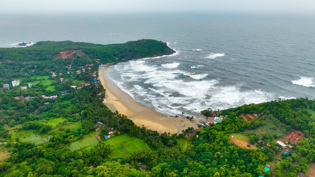 Aerial view of Gokarna Main Beach with waves crashing on the sandy shore surrounded by lush green vegetation and palm trees in Gokarna Karnataka India.