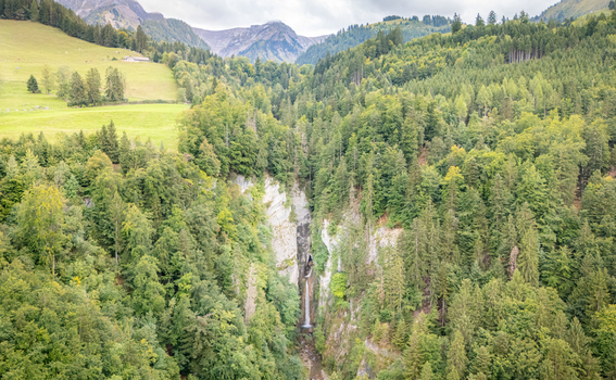 Aerial view of Grandvillard Waterfall cascading down a rocky cliff surrounded by dense green forest and alpine mountains in Grandvillard Fribourg Switzerland.