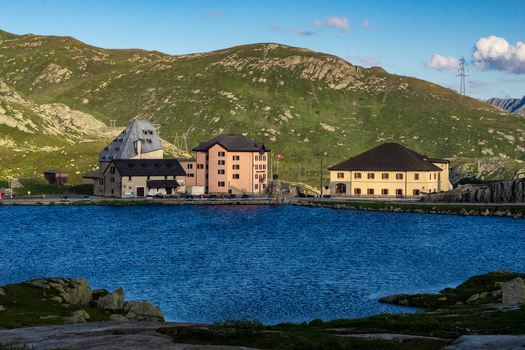 View of the historic buildings at Sankt Gotthard Pass overlooking the calm blue lake and green alpine mountains in Airolo Ticino Switzerland.