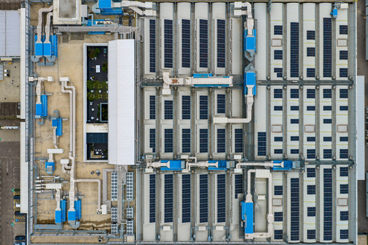 Aerial view of a large industrial rooftop featuring extensive solar panel arrays complex HVAC ventilation systems and a small green courtyard San Giovanni Valdarno Tuscany Italy.