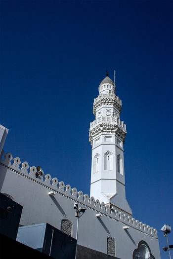 View of the white minaret and ornate parapet of the historic Masjid Quba mosque set against a clear deep blue sky in Madinah Al Madinah Province Saudi Arabia.