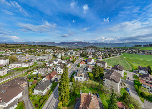 Aerial view of residential houses and apartment buildings surrounded by green fields and distant mountains under a blue sky in Biberist Solothurn Switzerland. Aerial view of residential houses and apartment buildings surrounded by green fields and distant mountains under a blue sky in Biberist Solothurn Switzerland.