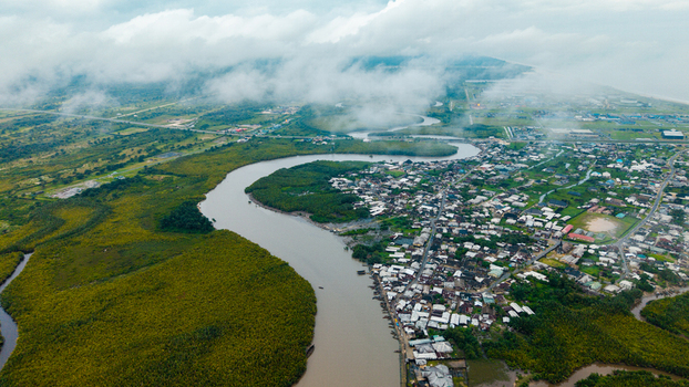 Aerial view of the winding Kwa Ibo River flowing through lush mangrove forests and a coastal settlement with dense housing under a cloudy sky in Kwa Ibo Akwa Ibom Nigeria.