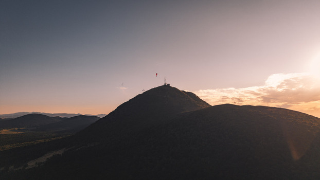 Aerial view of Puy de Dome at sunset with paragliders soaring above the volcanic mountain peak in Orcines Auvergne Rhone Alpes France.