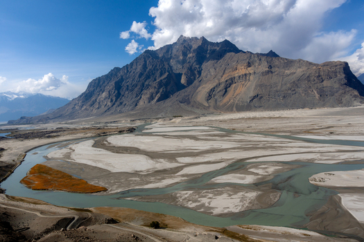 Aerial view of the Shigar Delta with its braided river channels sandy banks and rugged mountain backdrop under a blue sky in Shigar GB Pakistan. Aerial view of the Shigar Delta with its braided river channels sandy banks and rugged mountain backdrop under a blue sky in Shigar GB Pakistan.