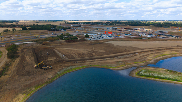 Aerial view of the construction site near the Black Cat Roundabout with blue water lakes in the foreground and heavy machinery in Chawston England United Kingdom.