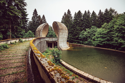View of the brutalist Korcanica Memorial Zone monument with curved concrete structures and a reflecting pool in a forest Sanski Most Federation of Bosnia Bosnia and Herzegovina. View of the brutalist Korcanica Memorial Zone monument with curved concrete structures and a reflecting pool in a forest Sanski Most Federation of Bosnia Bosnia and Herzegovina.